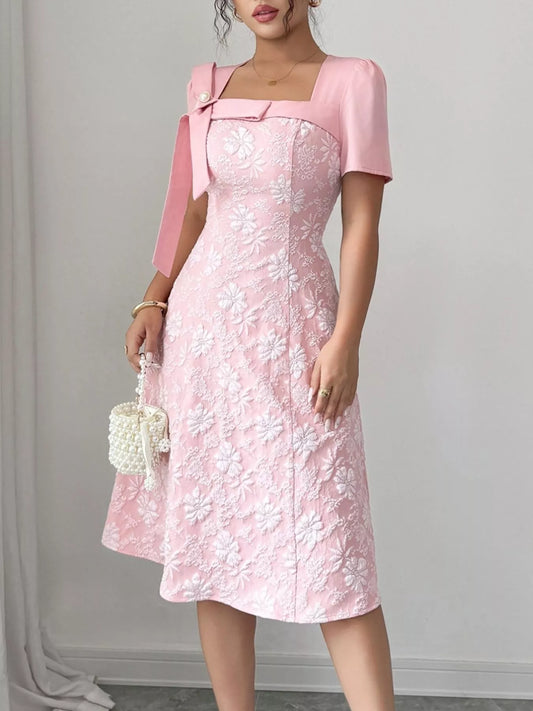 Woman wearing pink Cherry Blossom Charm Midi Dress with white floral embroidery and bow detail at shoulder, elegant midi party dress.