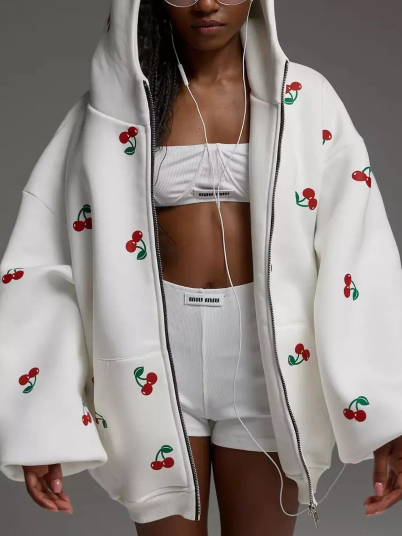 Model wearing a white oversized zip hoodie featuring red cherry embroidery and a front pocket, styled for a cute streetwear look.