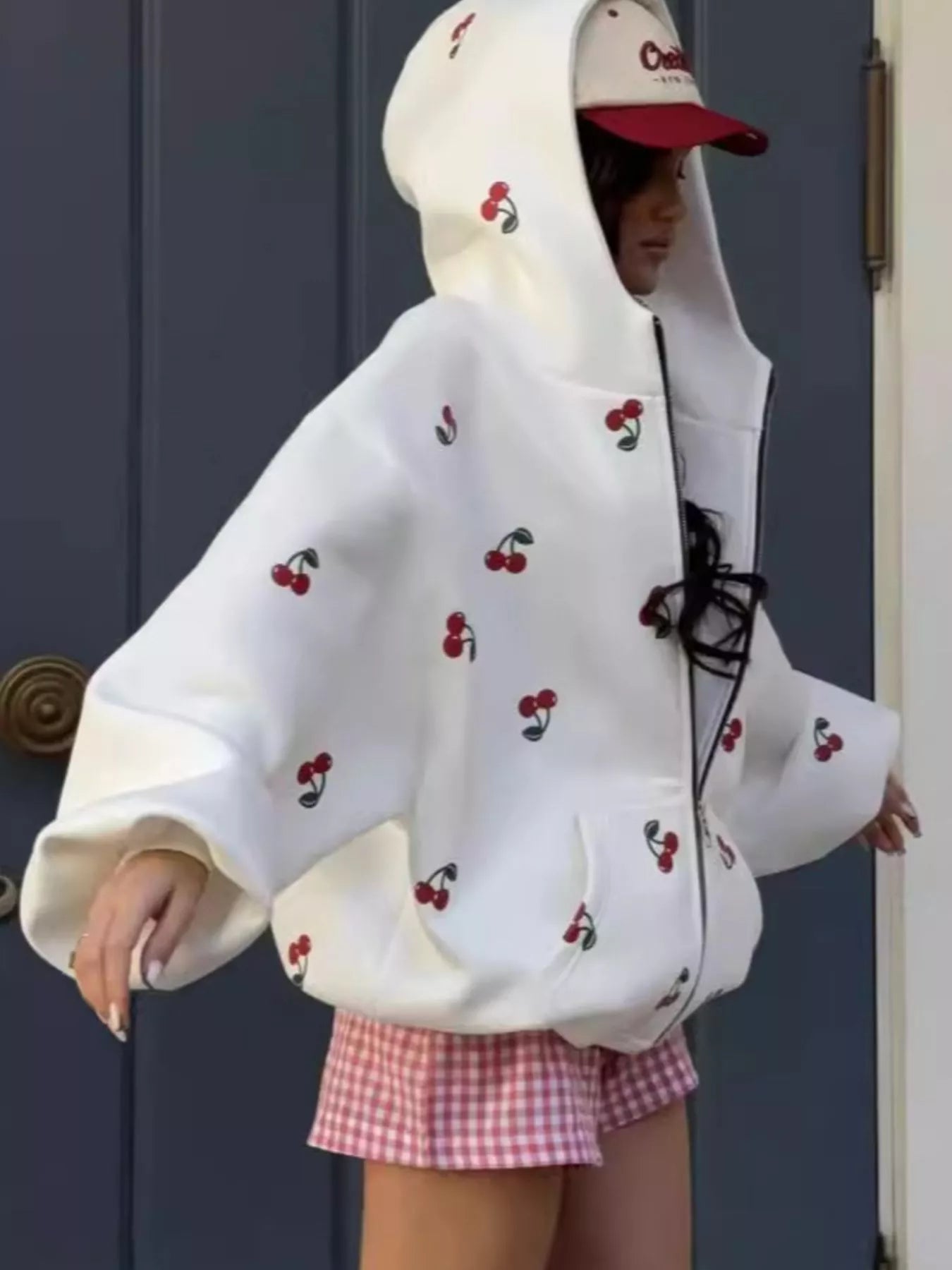 Model wearing a white oversized zip hoodie featuring red cherry embroidery and a front pocket, styled for a cute streetwear look.