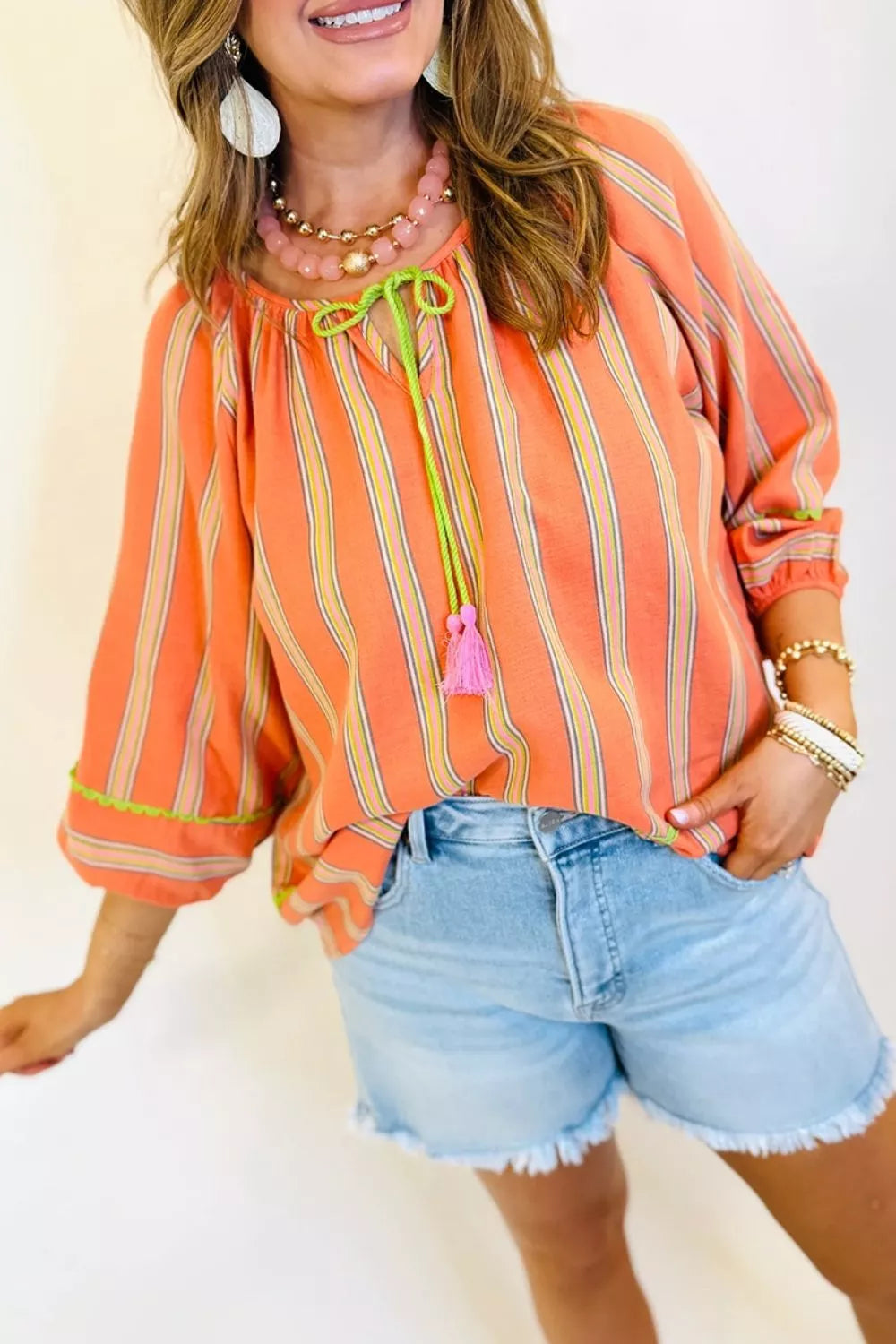 Bright striped cotton blouse with tie-front tassel detail, relaxed sleeves, and breezy boho style paired with denim shorts.