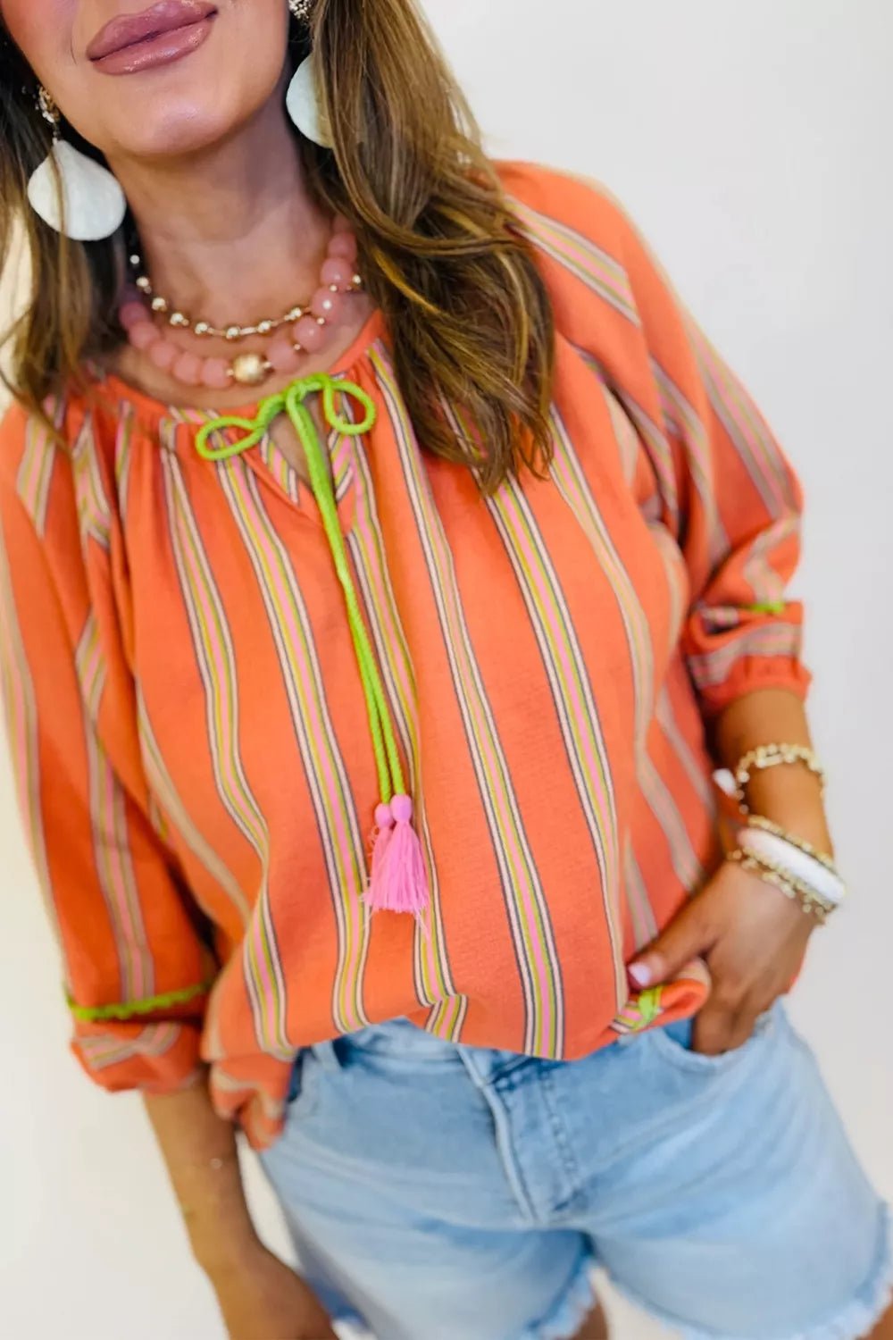 Bright striped cotton blouse with tie-front tassel detail, relaxed sleeves, and breezy boho style paired with denim shorts.