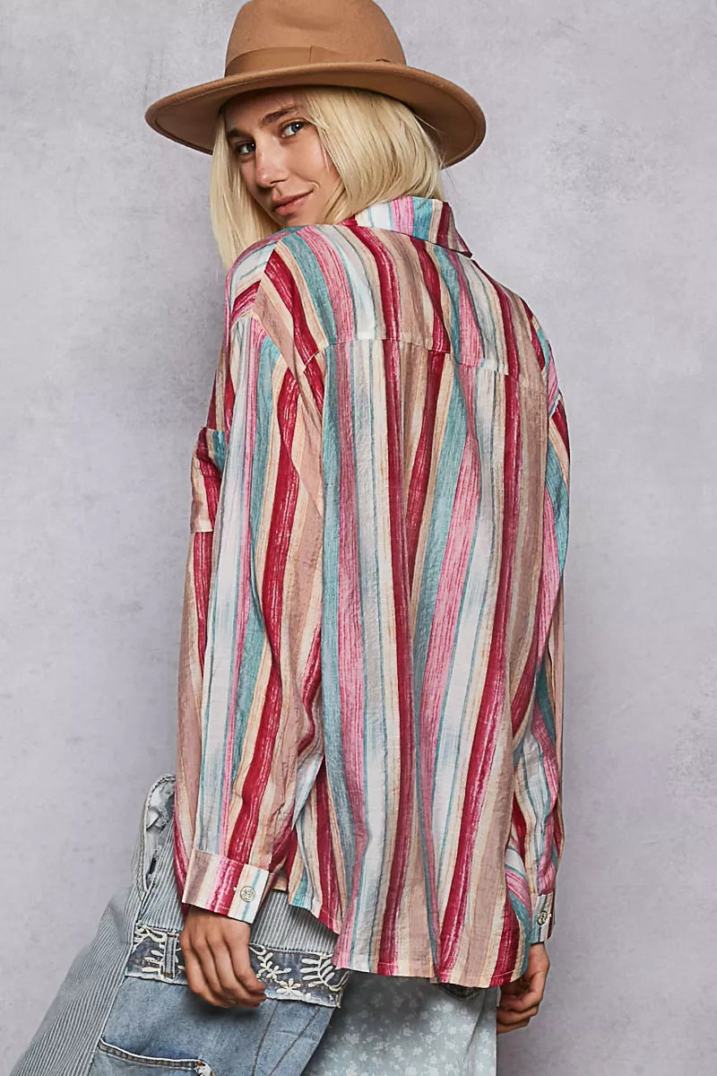 Woman wearing oversized striped button-down shirt in pink, teal, and cream hues with relaxed fit.