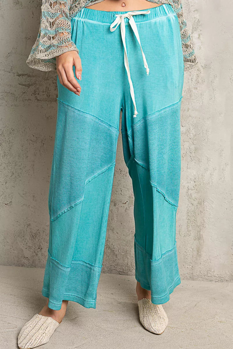 Model wearing teal ribbed wide-leg culotte pants with drawstring waist and textured contrast panels, styled casually with woven flats.