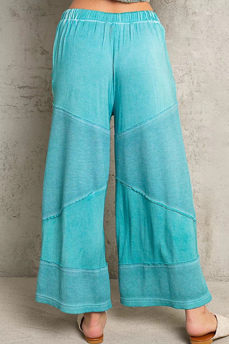 Model wearing teal ribbed wide-leg culotte pants with drawstring waist and textured contrast panels, styled casually with woven flats.