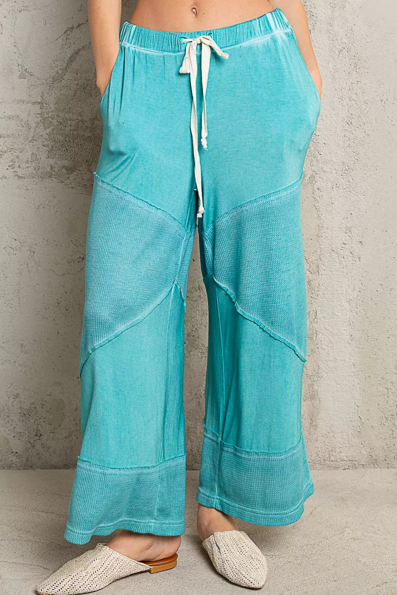 Model wearing teal ribbed wide-leg culotte pants with drawstring waist and textured contrast panels, styled casually with woven flats.
