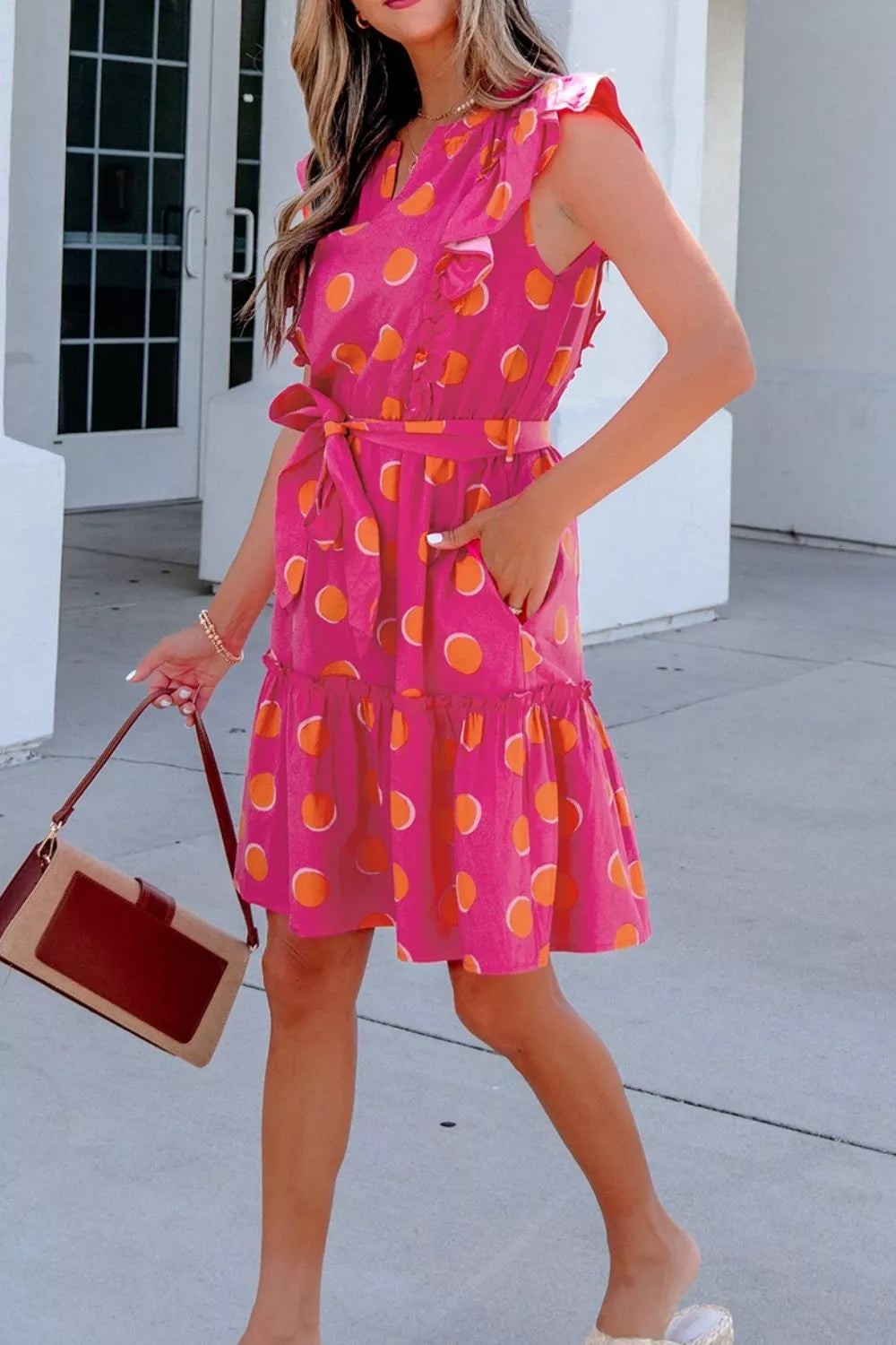 Bright polka dot mini dress with ruffled sleeves, belted waist, tiered skirt, and playful statement style.