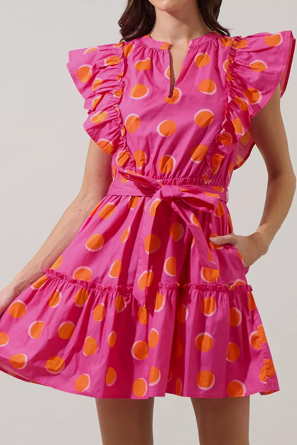 Bright polka dot mini dress with ruffled sleeves, belted waist, tiered skirt, and playful statement style.