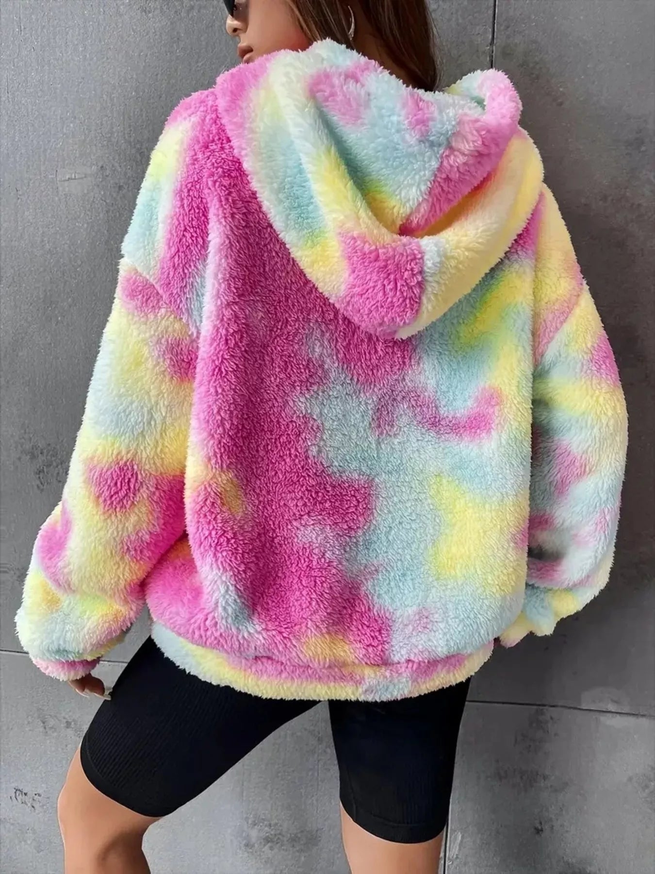 Model wearing a pastel tie-dye plush hoodie in pink, blue, and yellow with a kangaroo pocket and oversized cozy fit.