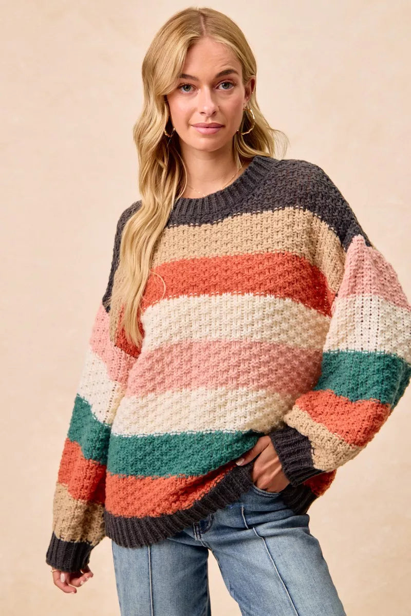 Woman wearing a Cozy Canyon Striped Chunky Sweater with bold color block stripes in earthy tones, styled with blue jeans for a casual winter look.