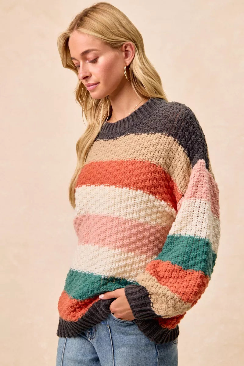 Woman wearing a Cozy Canyon Striped Chunky Sweater with bold color block stripes in earthy tones, styled with blue jeans for a casual winter look.