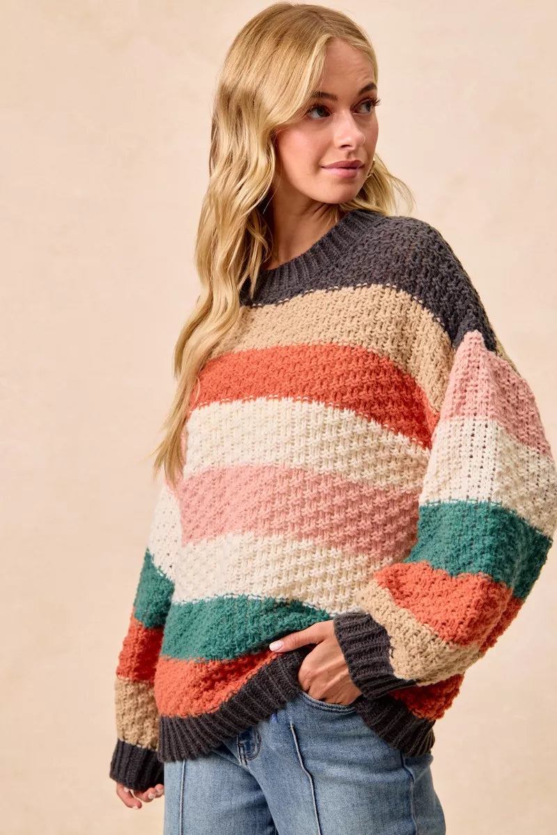 Woman wearing a Cozy Canyon Striped Chunky Sweater with bold color block stripes in earthy tones, styled with blue jeans for a casual winter look.