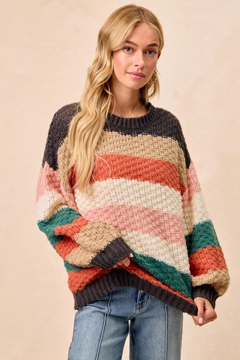 Woman wearing a Cozy Canyon Striped Chunky Sweater with bold color block stripes in earthy tones, styled with blue jeans for a casual winter look.