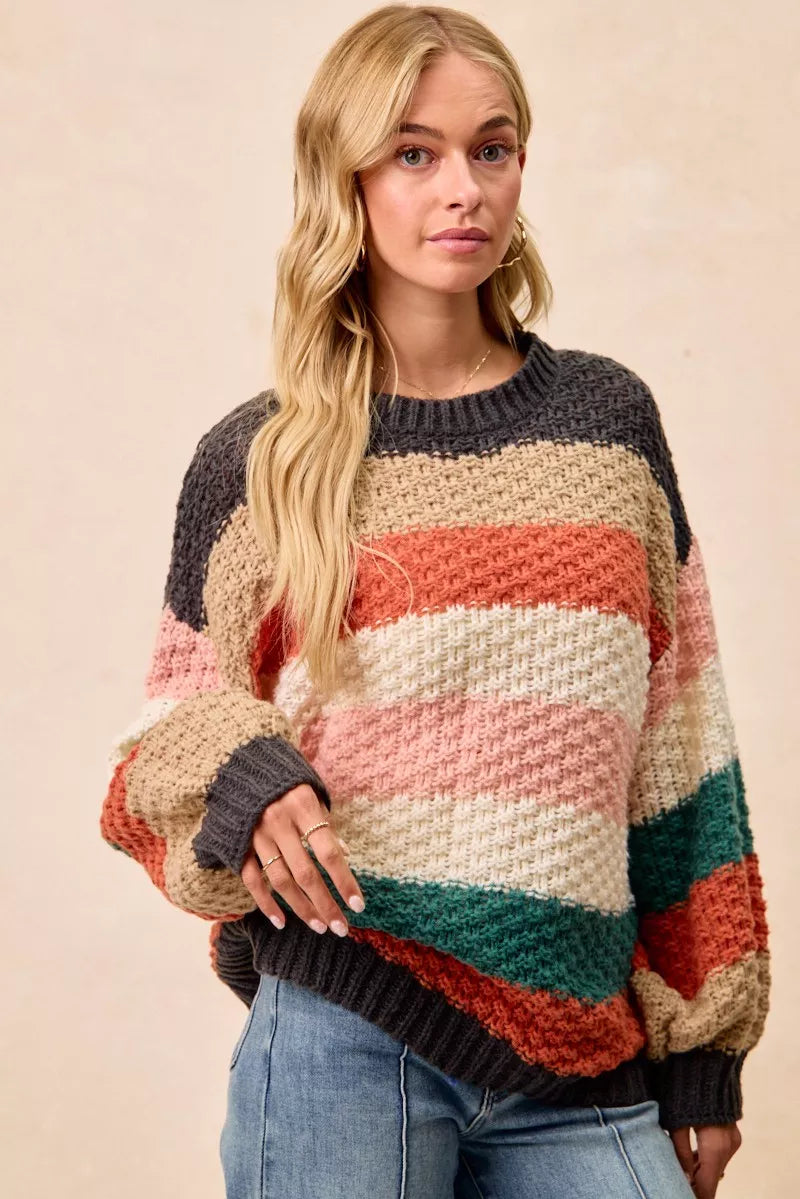 Woman wearing a Cozy Canyon Striped Chunky Sweater with bold color block stripes in earthy tones, styled with blue jeans for a casual winter look.