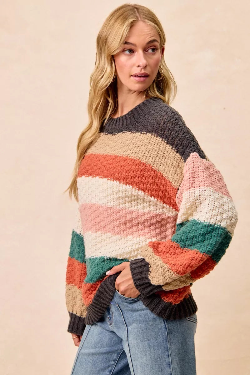 Woman wearing a Cozy Canyon Striped Chunky Sweater with bold color block stripes in earthy tones, styled with blue jeans for a casual winter look.