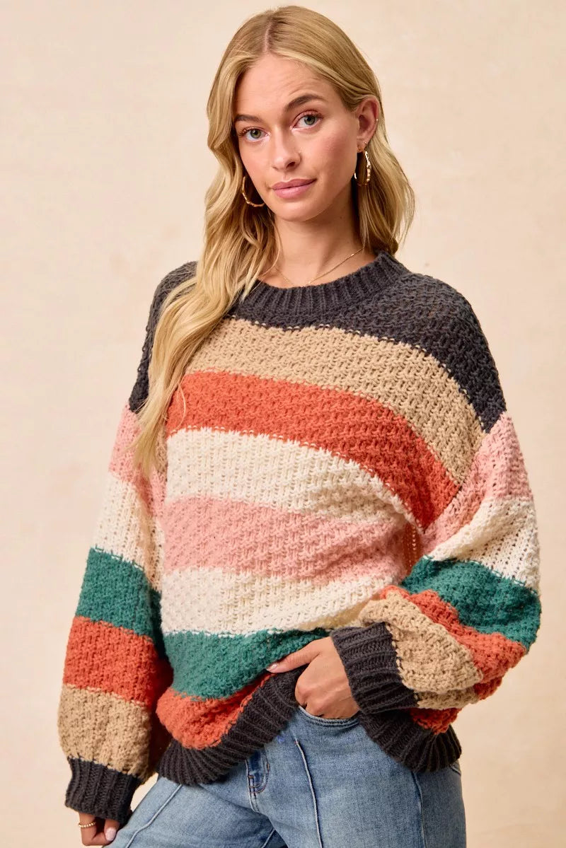 Woman wearing a Cozy Canyon Striped Chunky Sweater with bold color block stripes in earthy tones, styled with blue jeans for a casual winter look.