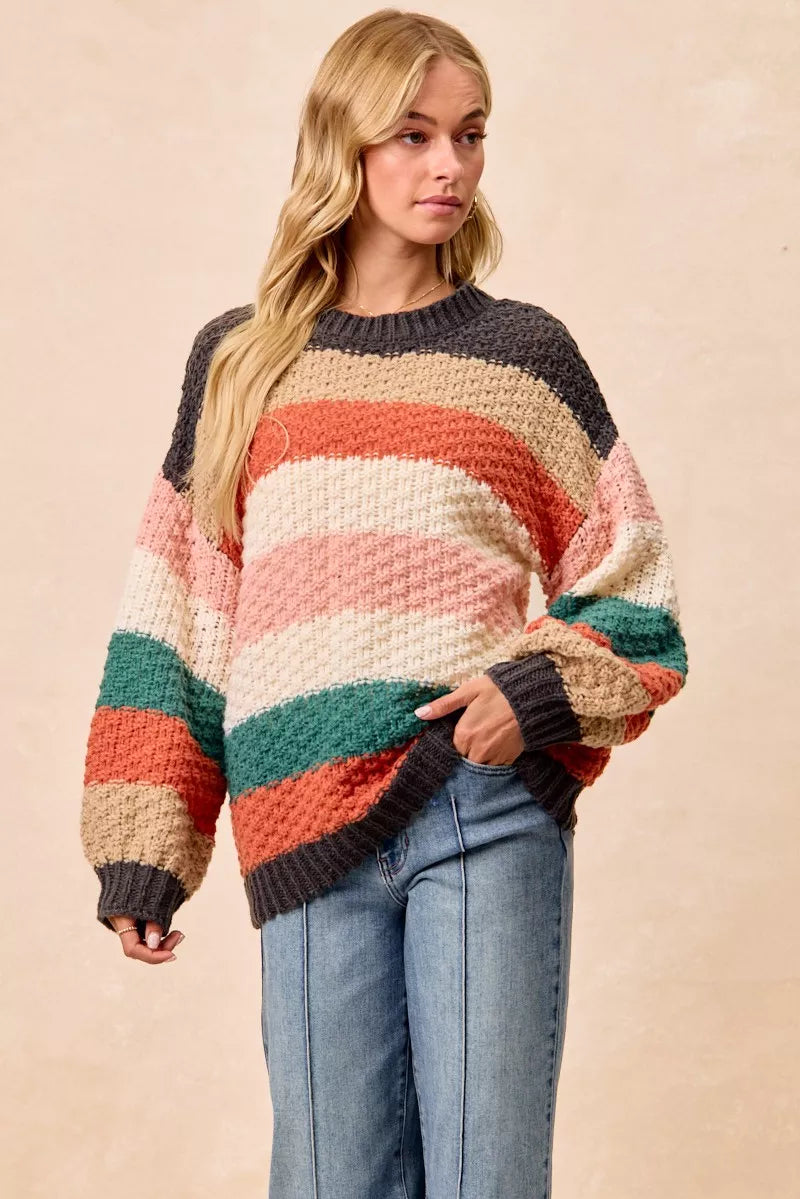 Woman wearing a Cozy Canyon Striped Chunky Sweater with bold color block stripes in earthy tones, styled with blue jeans for a casual winter look.