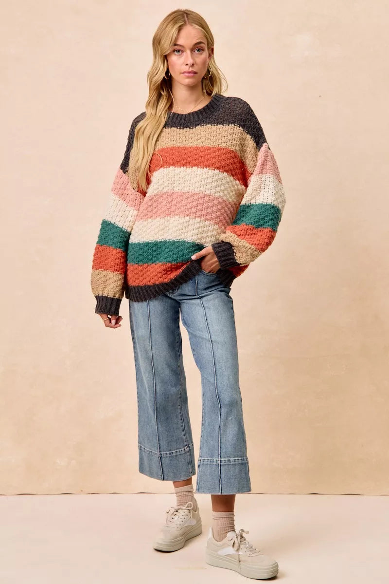 Woman wearing a Cozy Canyon Striped Chunky Sweater with bold color block stripes in earthy tones, styled with blue jeans for a casual winter look.