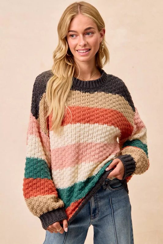Woman wearing a Cozy Canyon Striped Chunky Sweater with bold color block stripes in earthy tones, styled with blue jeans for a casual winter look.