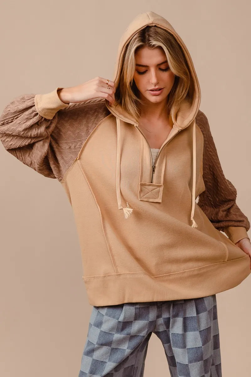 Woman wearing a beige French terry hoodie with knit sleeves and a half-zip front for a cozy, casual look.