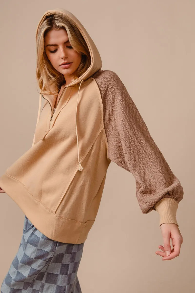 Woman wearing a beige French terry hoodie with knit sleeves and a half-zip front for a cozy, casual look.