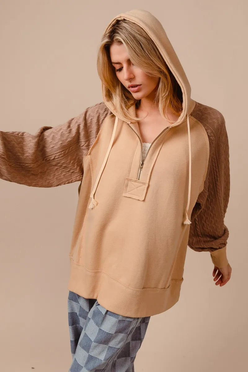 Woman wearing a beige French terry hoodie with knit sleeves and a half-zip front for a cozy, casual look.