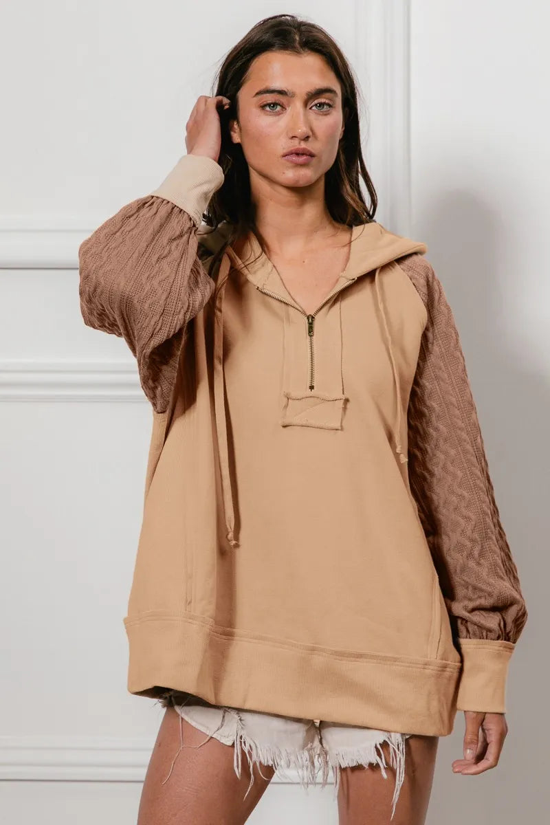 Woman wearing a beige French terry hoodie with knit sleeves and a half-zip front for a cozy, casual look.