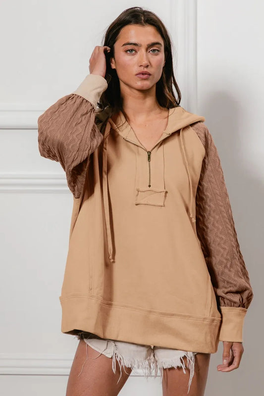 Woman wearing a beige French terry hoodie with knit sleeves and a half-zip front for a cozy, casual look.