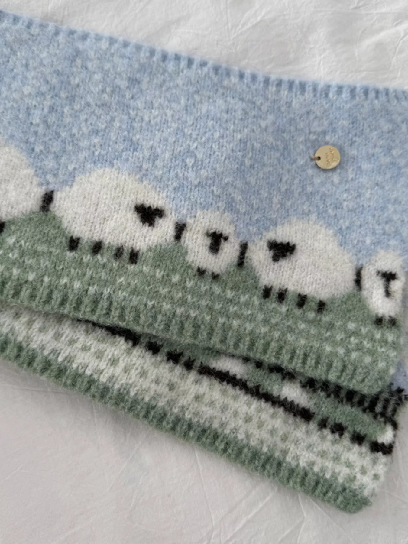 Soft knit scarf featuring a whimsical sheep pattern laid out on a neutral fabric background