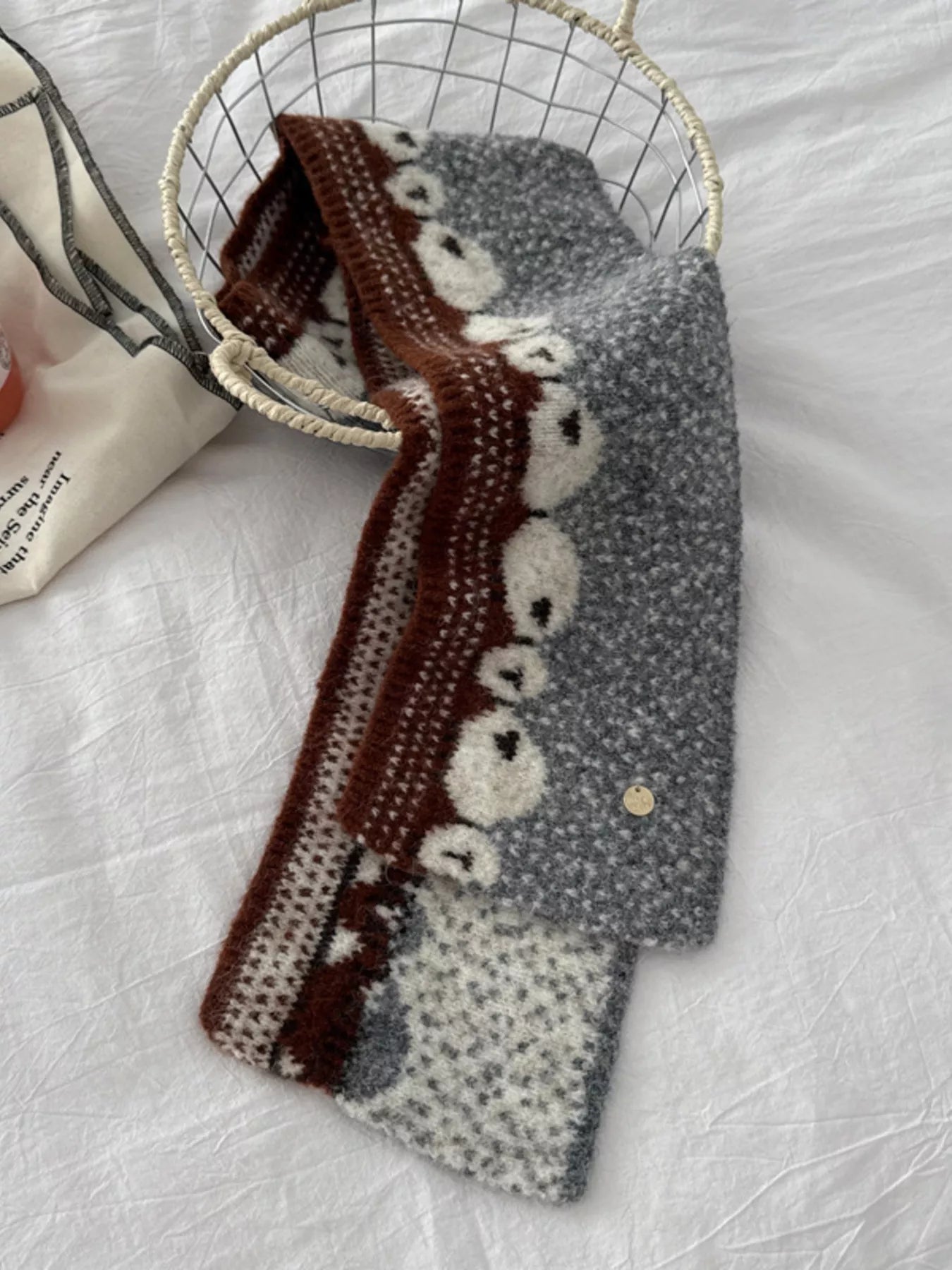 Soft knit scarf featuring a whimsical sheep pattern laid out on a neutral fabric background