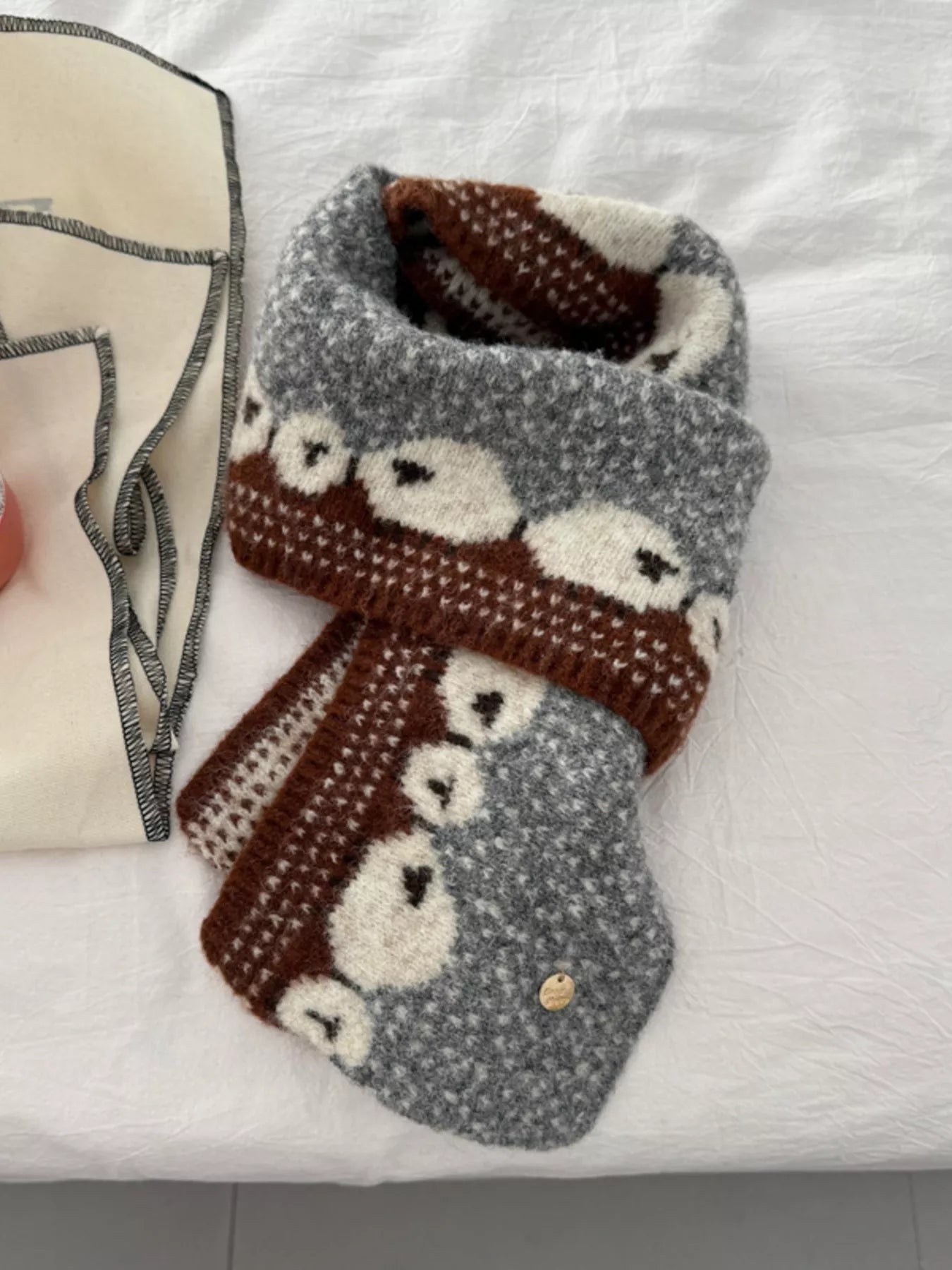 Soft knit scarf featuring a whimsical sheep pattern laid out on a neutral fabric background