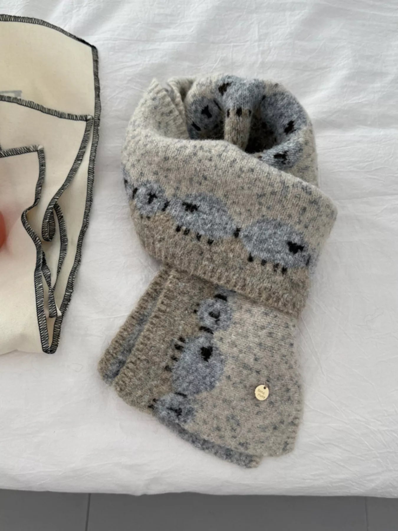 Soft knit scarf featuring a whimsical sheep pattern laid out on a neutral fabric background