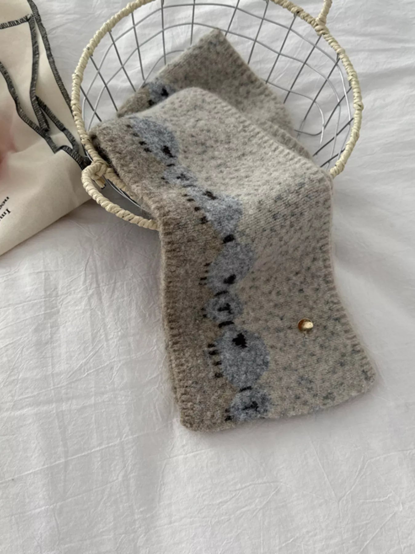 Soft knit scarf featuring a whimsical sheep pattern laid out on a neutral fabric background
