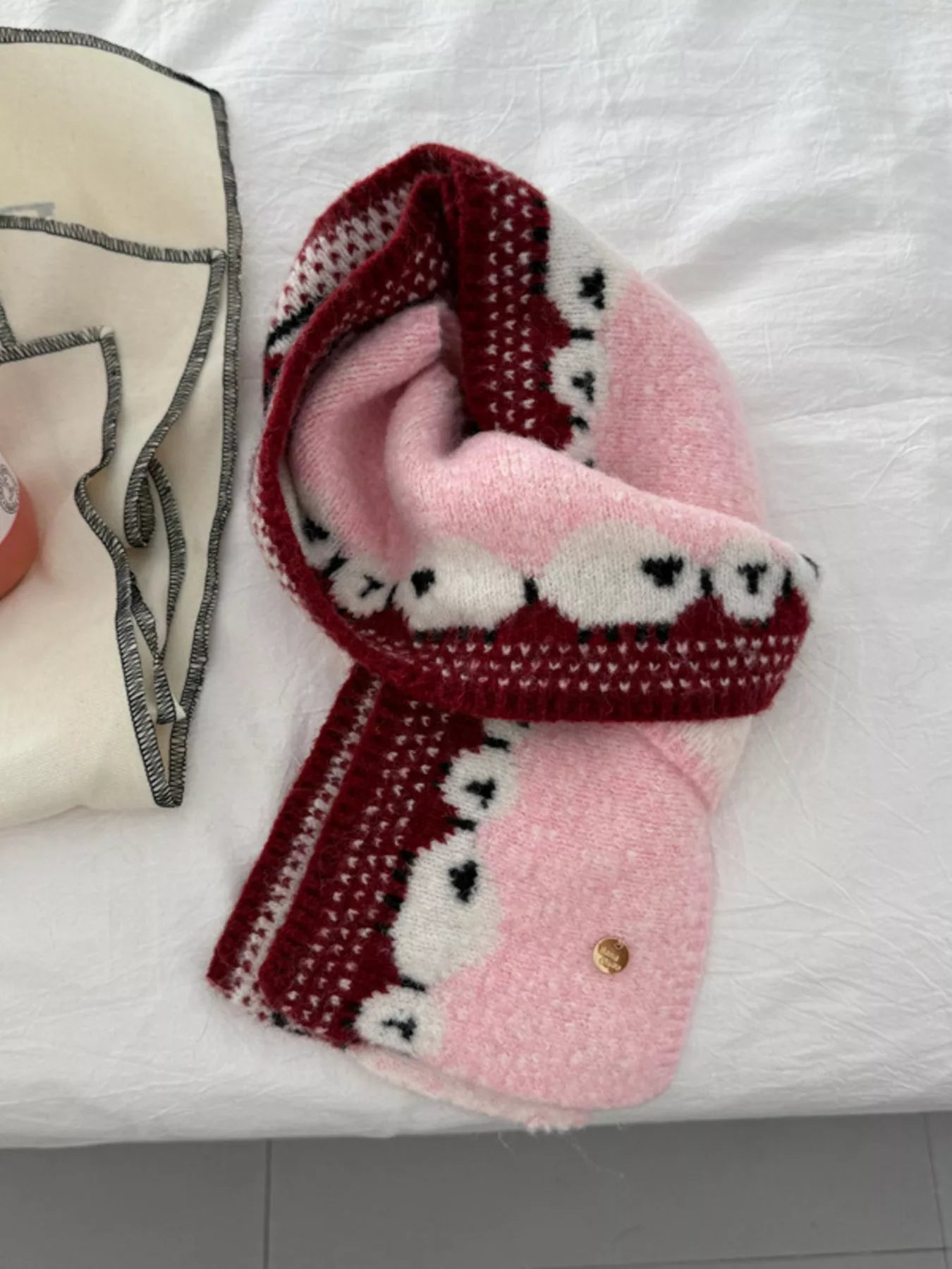 Soft knit scarf featuring a whimsical sheep pattern laid out on a neutral fabric background