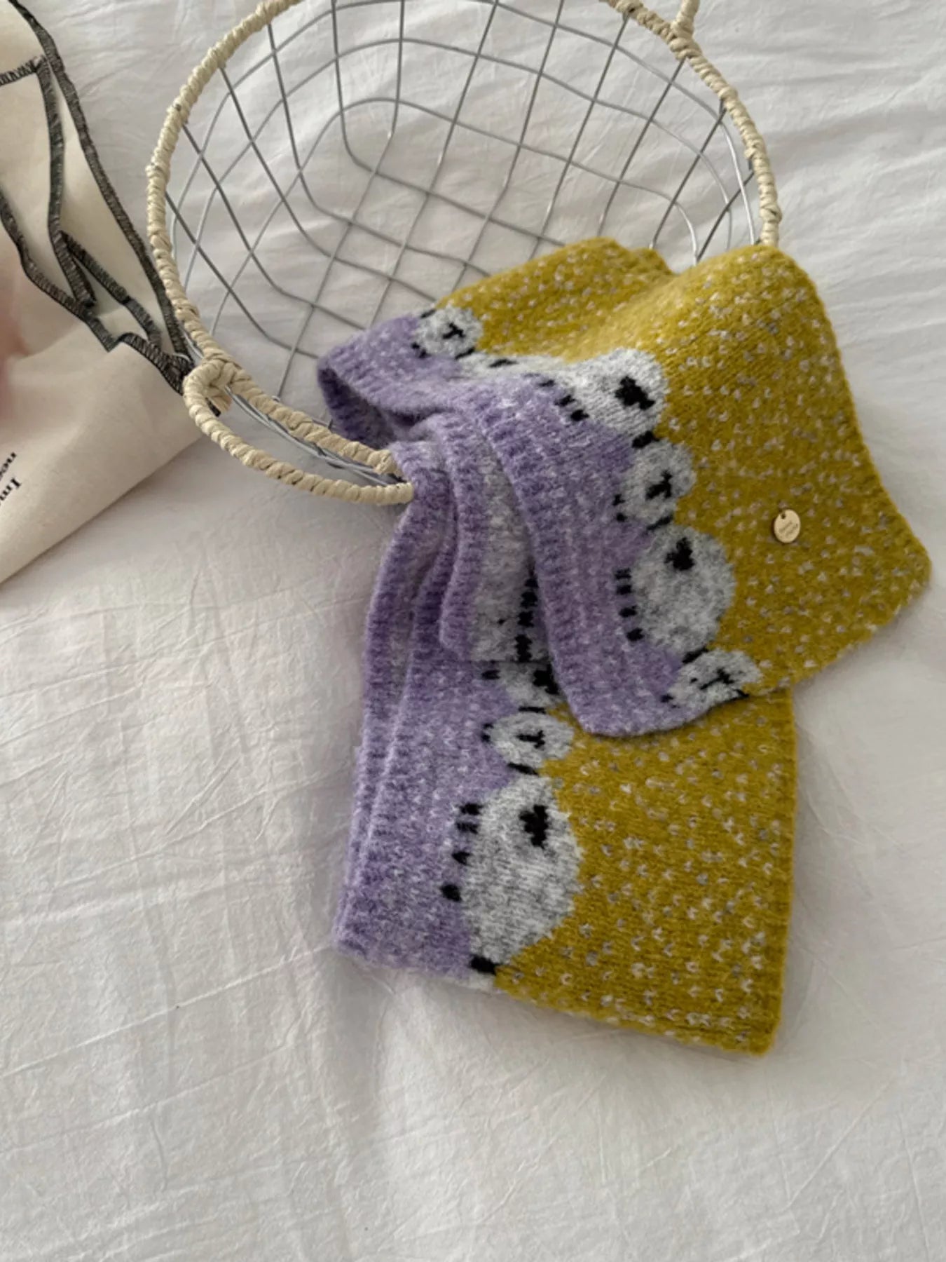 Soft knit scarf featuring a whimsical sheep pattern laid out on a neutral fabric background