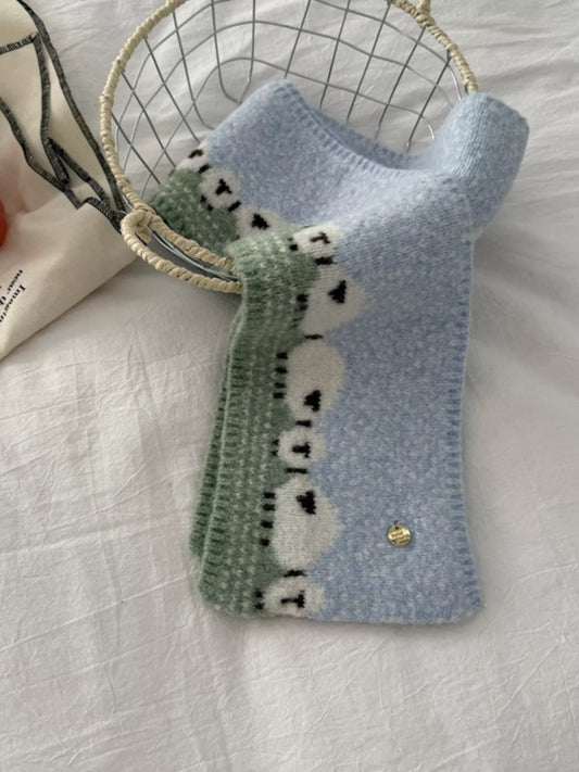 Soft knit scarf featuring a whimsical sheep pattern laid out on a neutral fabric background