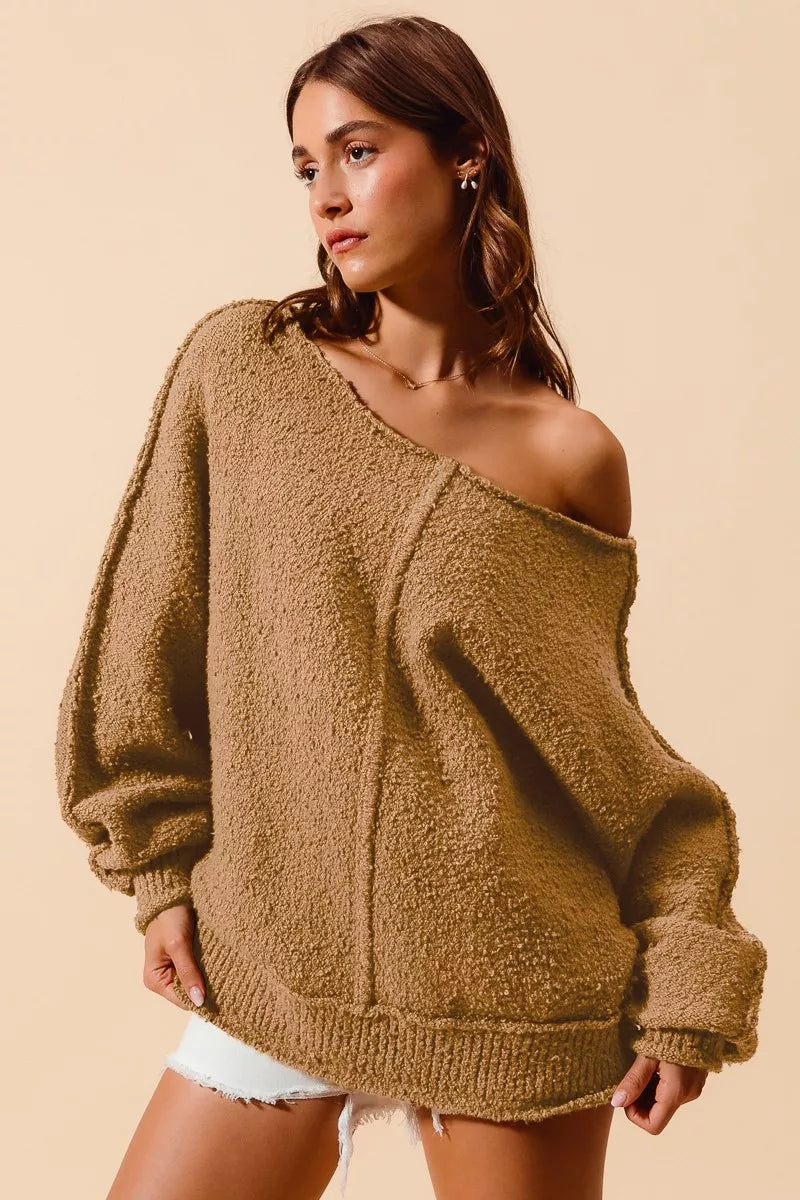 Model wearing an oversized tan bouclé sweater with exposed seam detailing and slouchy off-the-shoulder fit, styled casually with shorts for a cozy and relaxed look.