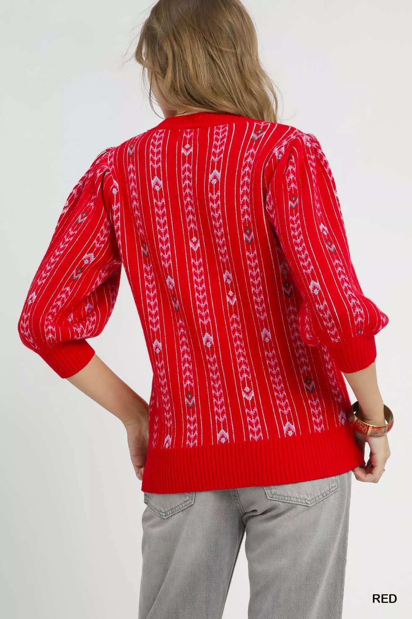 Woman wearing the Crimson Cascade Sweater in bold red with jacquard knit pattern and puff sleeves.