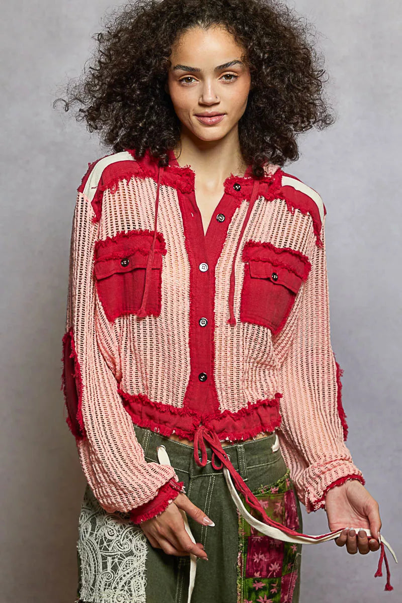 Model wearing a red and pink woven hooded button-down shirt with patch pockets and drawstring hem, styled with boho pants.