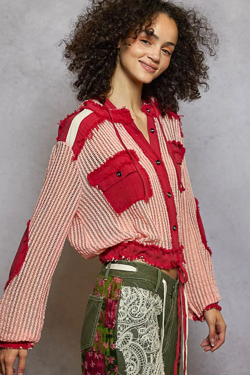 Model wearing a red and pink woven hooded button-down shirt with patch pockets and drawstring hem, styled with boho pants.