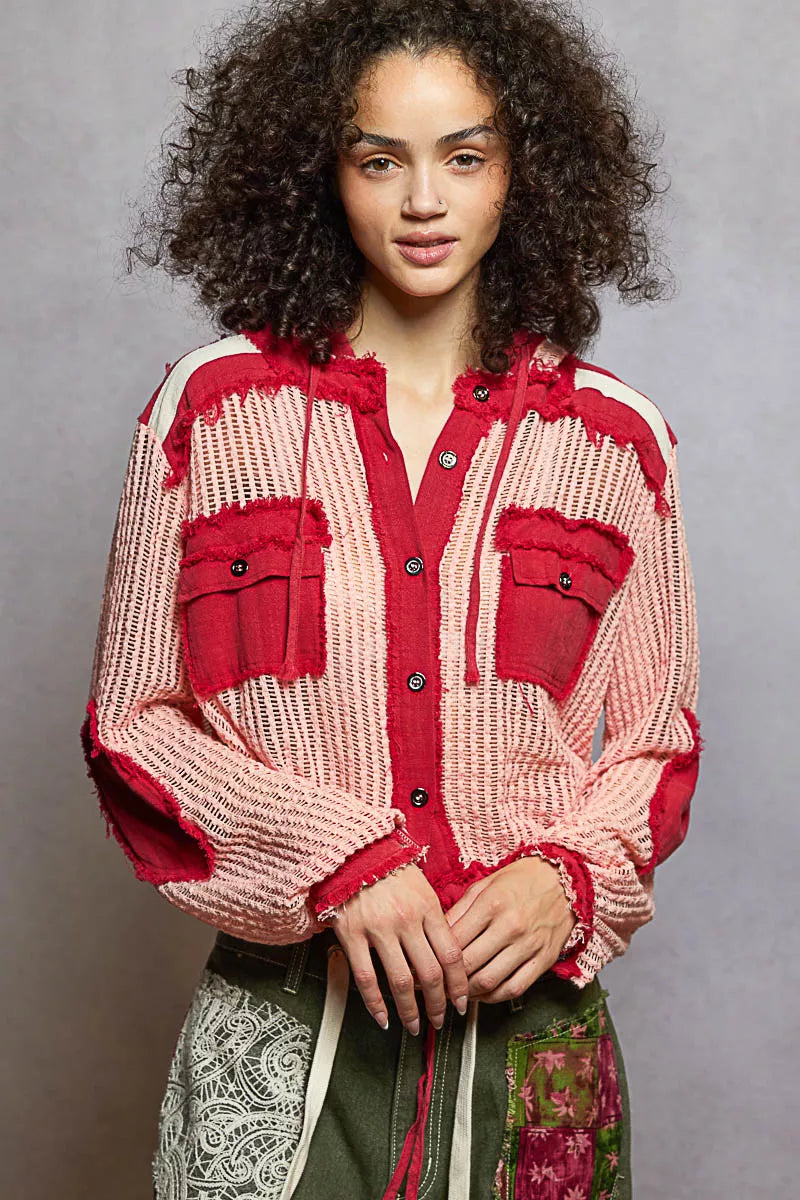 Model wearing a red and pink woven hooded button-down shirt with patch pockets and drawstring hem, styled with boho pants.