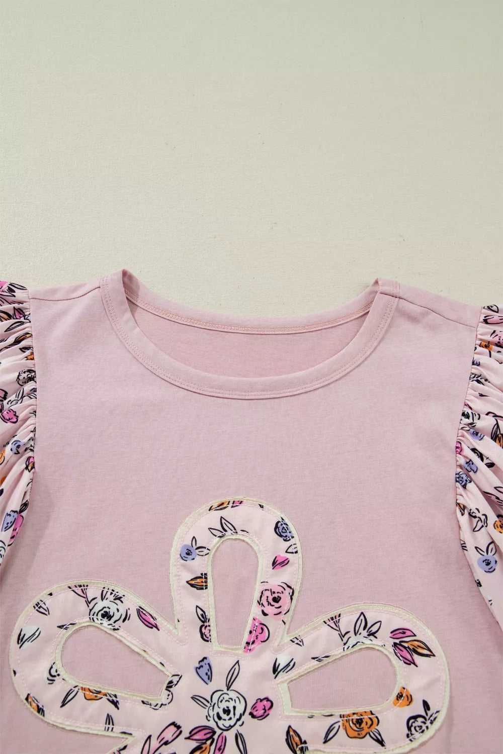 Light pink tee with floral puff sleeves and an oversized floral appliqué on the front styled with denim shorts.