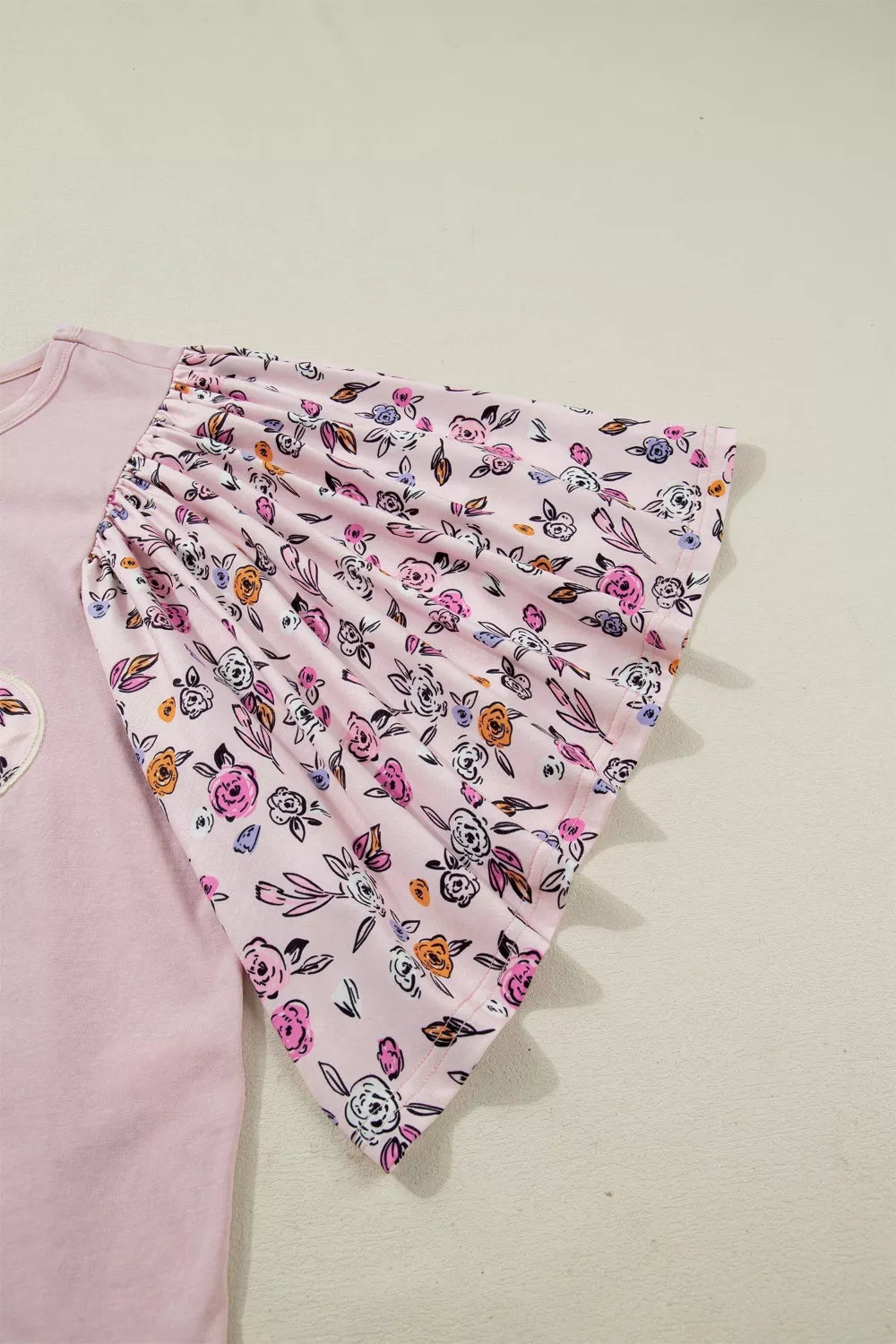 Light pink tee with floral puff sleeves and an oversized floral appliqué on the front styled with denim shorts.