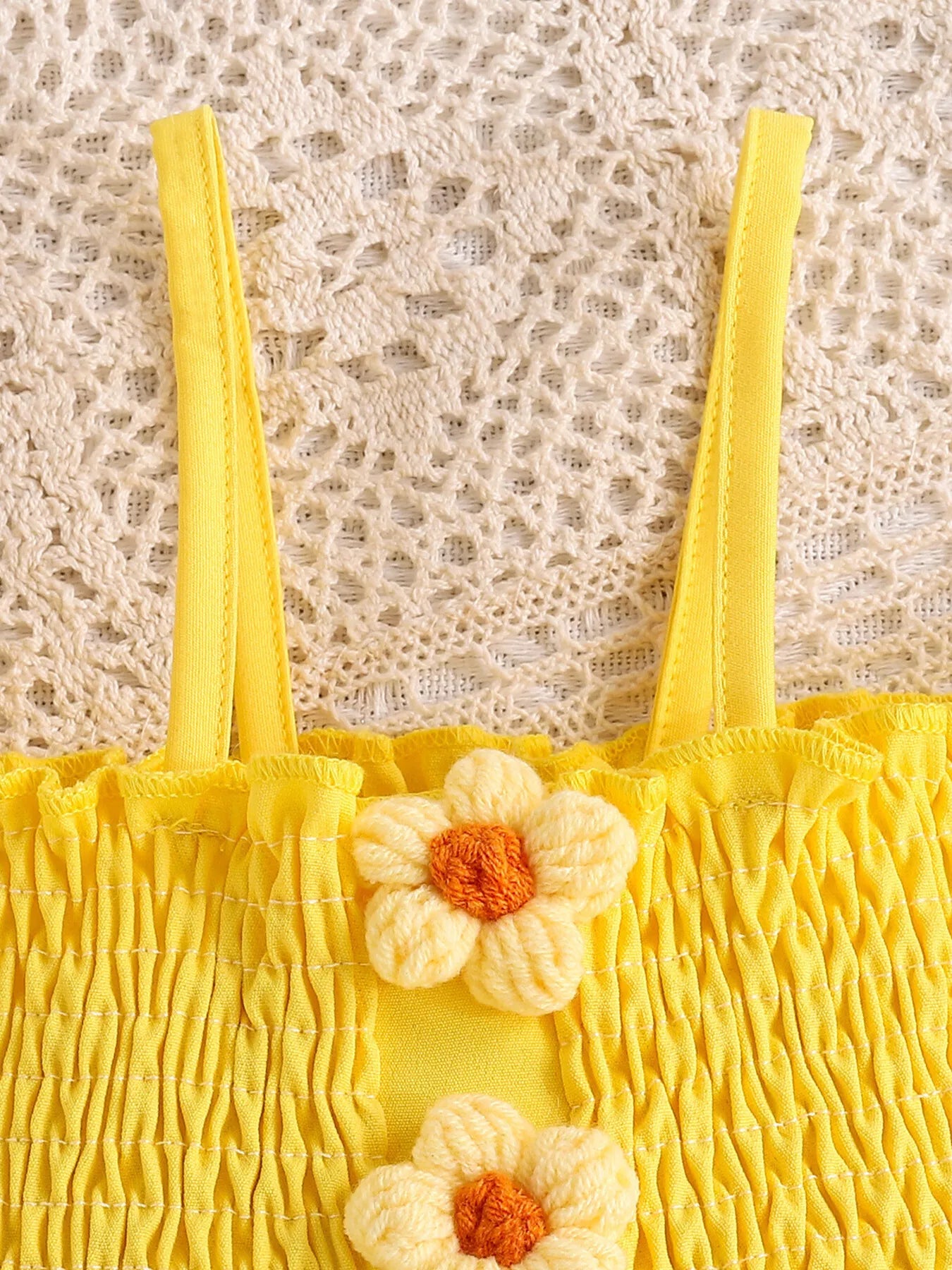 Yellow toddler romper with smocked bodice, daisy appliqué details, ruffled sleeves, pockets, and soft cotton-blend fabric.