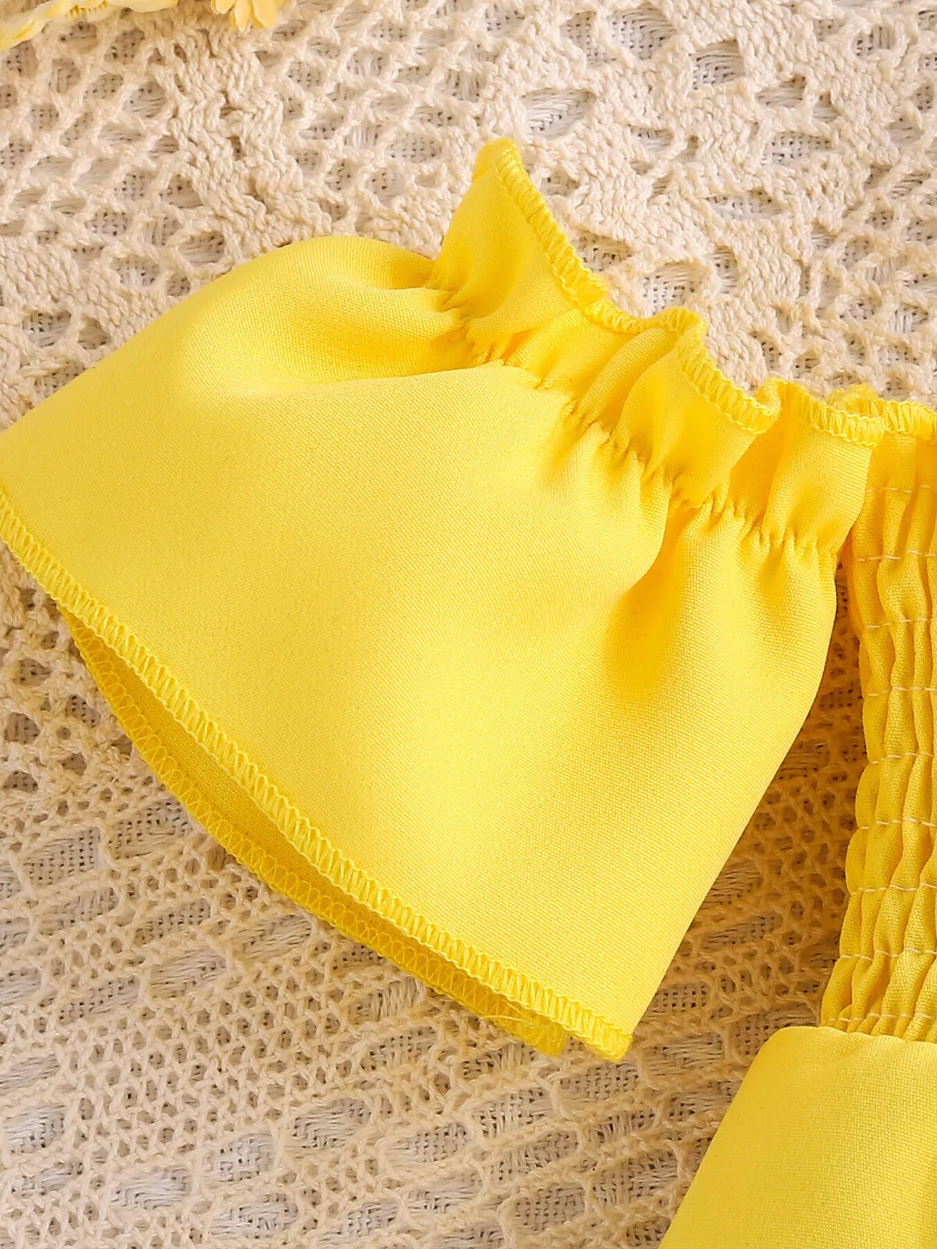 Yellow toddler romper with smocked bodice, daisy appliqué details, ruffled sleeves, pockets, and soft cotton-blend fabric.