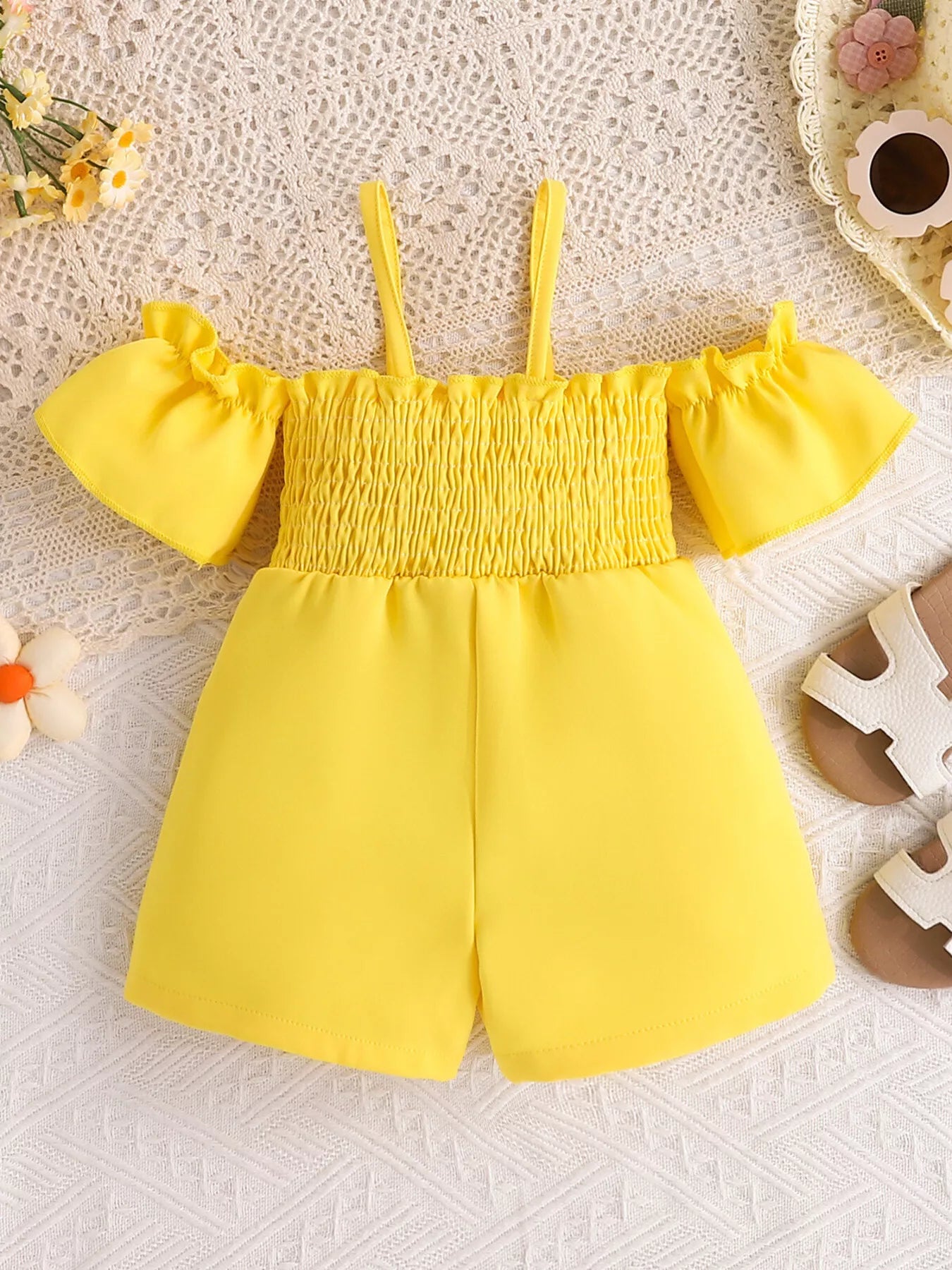 Yellow toddler romper with smocked bodice, daisy appliqué details, ruffled sleeves, pockets, and soft cotton-blend fabric.