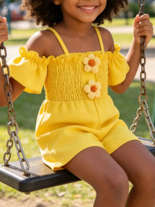 Yellow toddler romper with smocked bodice, daisy appliqué details, ruffled sleeves, pockets, and soft cotton-blend fabric.