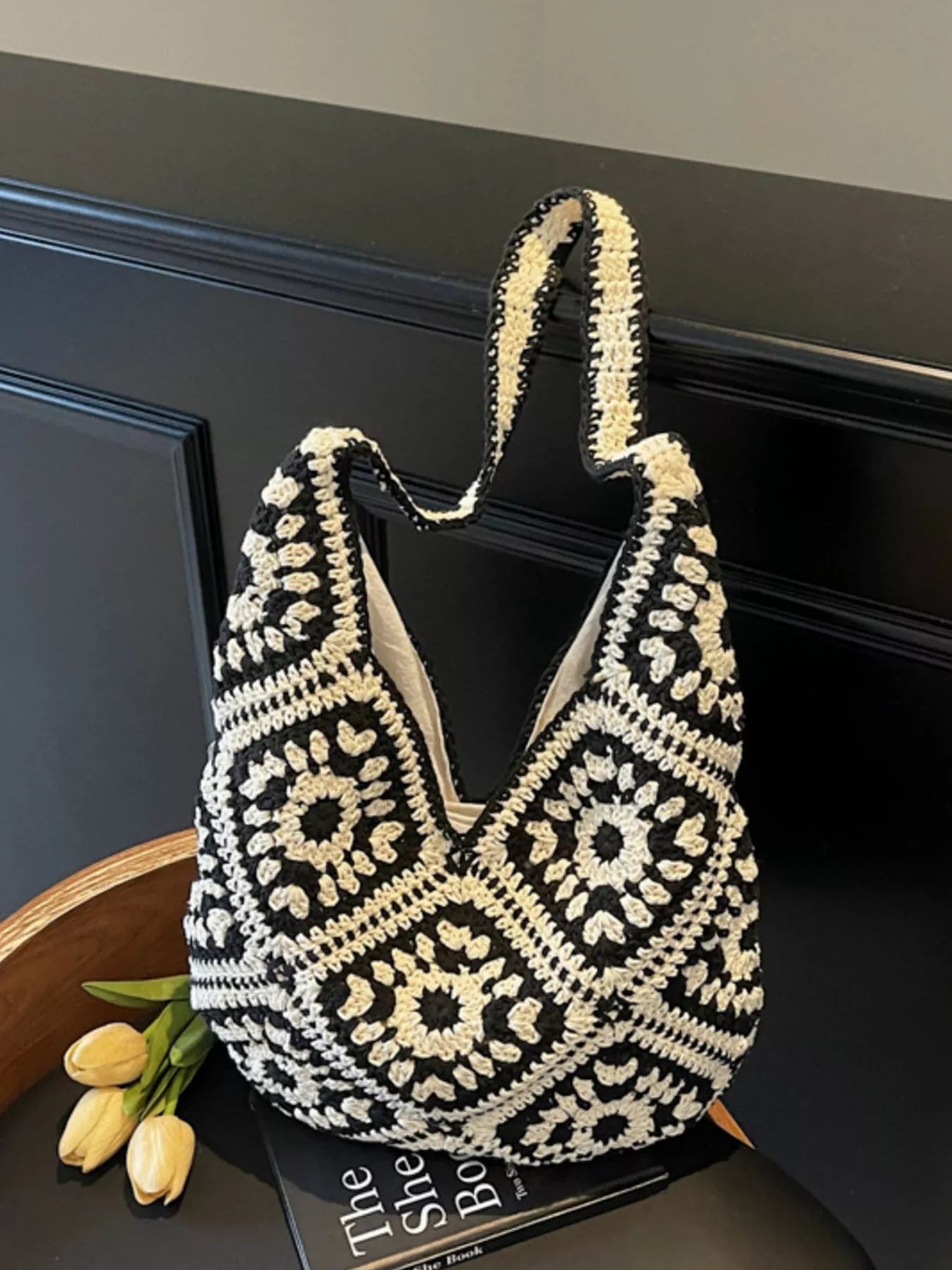 Black and cream crochet shoulder bag with a floral square pattern and roomy large silhouette worn over the shoulder.