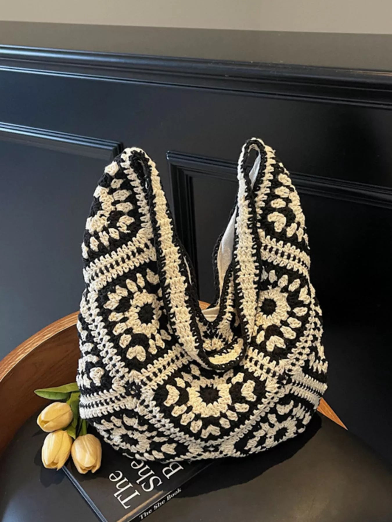 Black and cream crochet shoulder bag with a floral square pattern and roomy large silhouette worn over the shoulder.