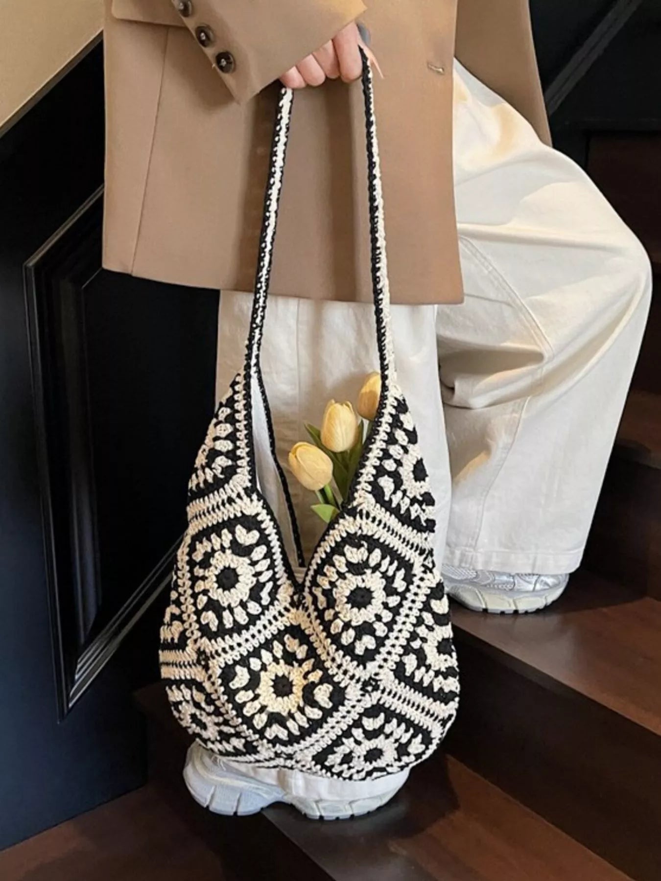 Black and cream crochet shoulder bag with a floral square pattern and roomy large silhouette worn over the shoulder.