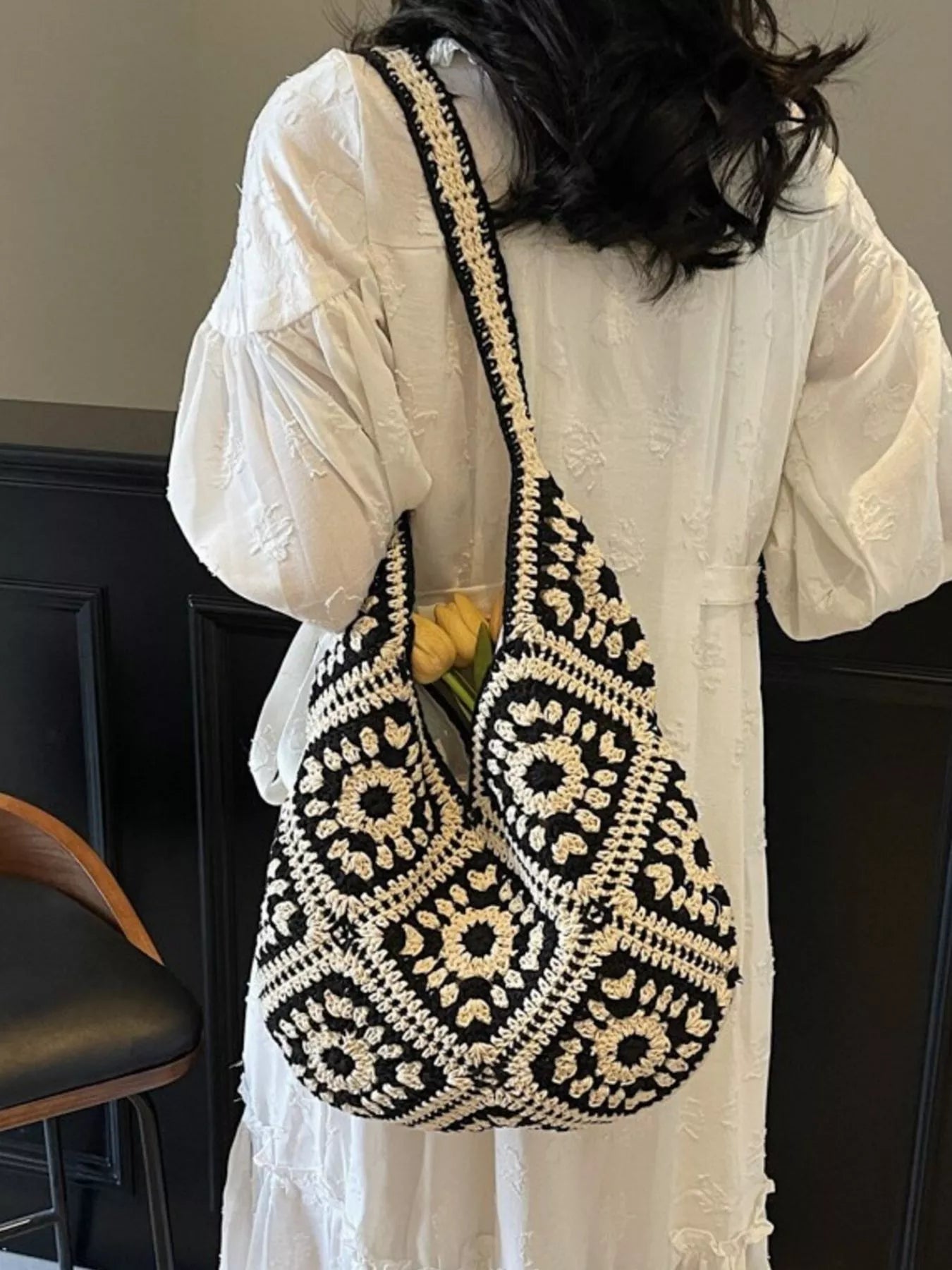 Black and cream crochet shoulder bag with a floral square pattern and roomy large silhouette worn over the shoulder.